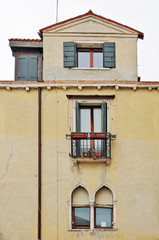 Fototapeta na wymiar Yellow wall of an old house with windows and a balcony in Venetian style