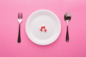 Dietary supplement on plate with fork and spoon on pink background