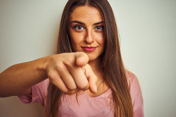 Young beautiful woman wearing pink t-shirt standing over isolated white background pointing with finger to the camera and to you, hand sign, positive and confident gesture from the front