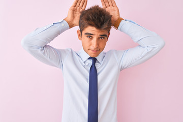 Young handsome businessman wearing shirt and tie standing over isolated pink background Doing bunny ears gesture with hands palms looking cynical and skeptical. Easter rabbit concept.