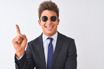 Young handsome businessman wearing suit and sunglasses over isolated white background with a big smile on face, pointing with hand and finger to the side looking at the camera.