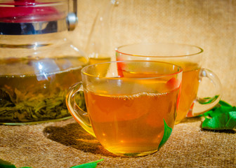 glass teapot and two cup of green tea or black tea with fresh leaves on the back of a traditional background sackcloth