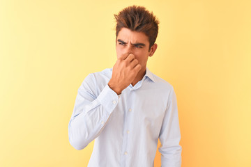 Young handsome businessman wearing elegant shirt over isolated yellow background smelling something stinky and disgusting, intolerable smell, holding breath with fingers on nose. Bad smells concept.