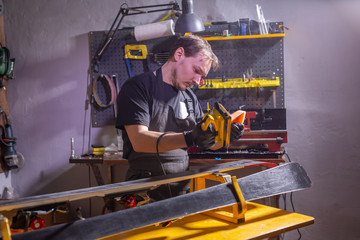 Fototapeta na wymiar A man in work clothes repairman in the workshop ski service repairing the ski