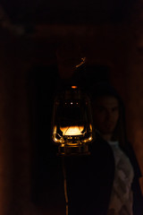 Fototapeta na wymiar Portrait of man in hoodie holding out an old vintage kerosene lantern in his hand in the dark close up