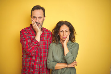 Beautiful middle age couple over isolated yellow background thinking looking tired and bored with depression problems with crossed arms.