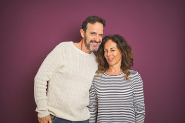 Beautiful middle age couple wearing winter sweater over isolated purple background winking looking at the camera with sexy expression, cheerful and happy face.