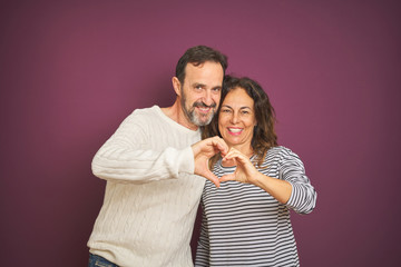 Naklejka premium Beautiful middle age couple wearing winter sweater over isolated purple background smiling in love doing heart symbol shape with hands. Romantic concept.