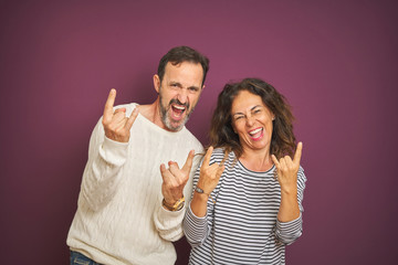 Beautiful middle age couple wearing winter sweater over isolated purple background shouting with crazy expression doing rock symbol with hands up. Music star. Heavy concept.