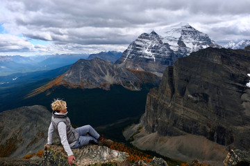 Naklejka premium Successful woman hiker sitting on mountain top enjoying view of mountain valley with yellow larch trees from above. Lake Louise area. Banff National park. Alberta. Canada.