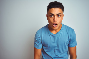 Young brazilian man wearing blue t-shirt standing over isolated white background afraid and shocked with surprise expression, fear and excited face.