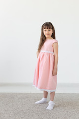 Beautiful little brunette girl in a pink dress posing on a white background. The concept of cute children. Copy space