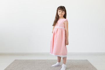 Beautiful little brunette girl in a pink dress posing on a white background. The concept of cute children. Copy space