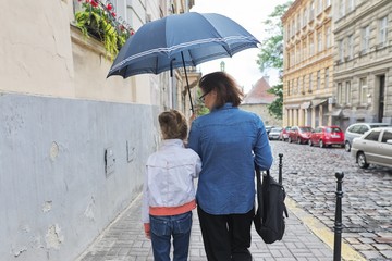 Woman with child girl walking under an umbrella in street