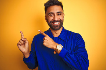 Handsome indian worker man wearing uniform over isolated yellow background smiling and looking at the camera pointing with two hands and fingers to the side.