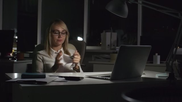 Medium shot of overworked businesswoman brainstorming ideas in dark office while working after hours. She is writing something on sheet of paper, then crumpling it and throwing towards camera