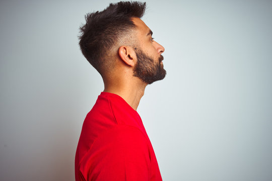 Young indian man wearing red t-shirt over isolated white background looking to side, relax profile pose with natural face with confident smile.