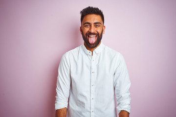 Young indian businessman wearing elegant shirt standing over isolated pink background sticking tongue out happy with funny expression. Emotion concept.
