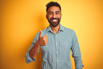 Young indian man wearing green striped shirt standing over isolated yellow background doing happy...
