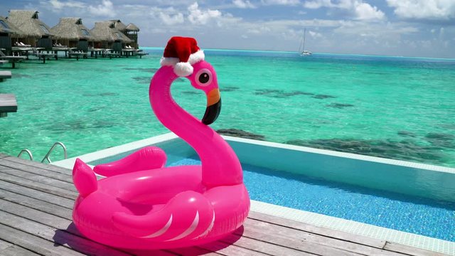 Christmas beach vacation flamingo pool float with santa hat travel background for winter holidays luxury getaway holiday.