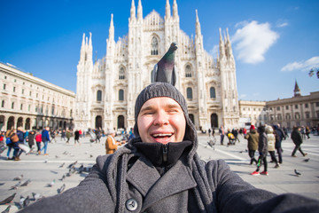 Winter travel, vacations and birds concept - Handsome male tourist with funny pigeons making selfie photo in front of the famous Duomo cathedral in Milan.