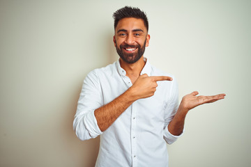 Young indian man wearing elegant shirt standing over isolated white background amazed and smiling to the camera while presenting with hand and pointing with finger.