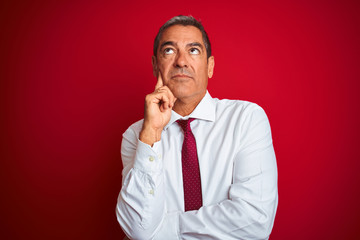 Handsome middle age businessman standing over isolated red background with hand on chin thinking about question, pensive expression. Smiling with thoughtful face. Doubt concept.