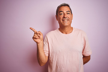 Handsome middle age man wearing t-shirt standing over isolated pink background with a big smile on face, pointing with hand and finger to the side looking at the camera.