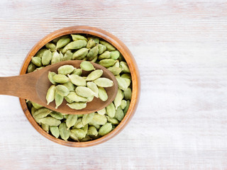 Spice Green cardamom (Elettaria cardamomum) in a wooden cup and spoon on a white wooden background
