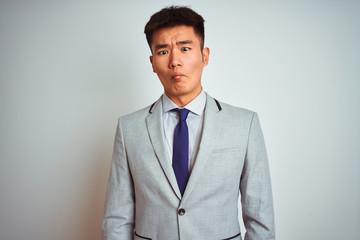 Asian chinese businessman wearing suit and tie standing over isolated yellow background making fish face with lips, crazy and comical gesture. Funny expression.