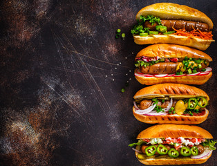 Hot dogs with different toppings on dark background, copy space, top view. Fast food concept.