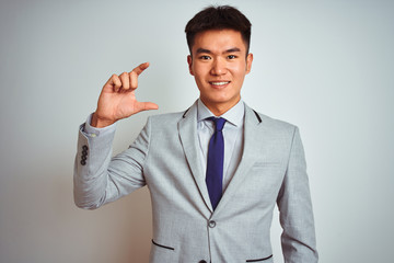 Asian chinese businessman wearing grey jacket and tie standing over isolated white background smiling and confident gesturing with hand doing small size sign