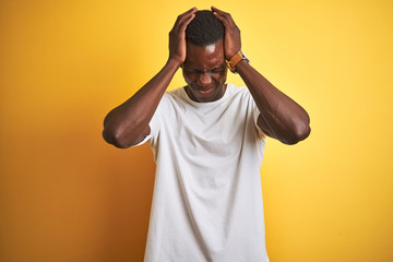 Fototapeta na wymiar Young african american man wearing white t-shirt standing over isolated yellow background suffering from headache desperate and stressed because pain and migraine. Hands on head.