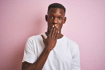 African american man wearing white t-shirt standing over isolated pink background cover mouth with hand shocked with shame for mistake, expression of fear, scared in silence, secret concept