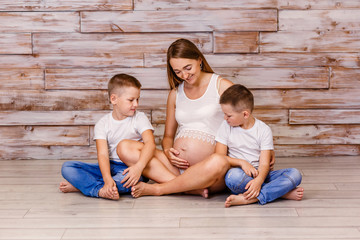 smiling pregnant woman with two children sitting on the floor on a wooden background in the Studio....