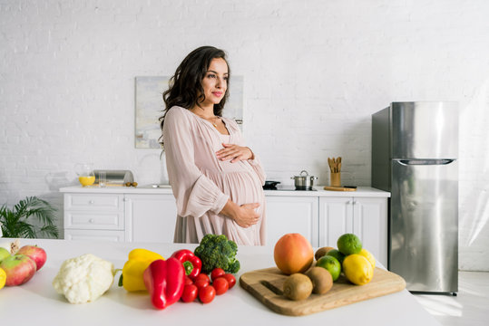 happy pregnant woman touching belly near tasty food on table