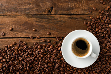 Overhead shot of hot coffee cup with beans on wooden background with copyspace
