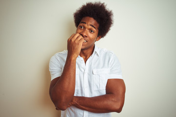 Fototapeta na wymiar African american man with afro hair wearing shirt standing over isolated white background looking stressed and nervous with hands on mouth biting nails. Anxiety problem.