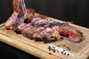 Medium-roasted steak cut into pieces on a wooden board with sauce and seasonings. Delicious steak. Beef steak medium rare on vegetable cushion. Beef steak on wooden plate. 