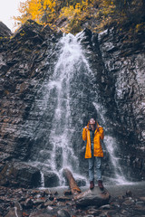 woman in yellow raincoat at autumn waterfall