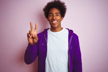 Young african american man wearing purple sweatshirt standing over isolated pink background showing and pointing up with fingers number two while smiling confident and happy.