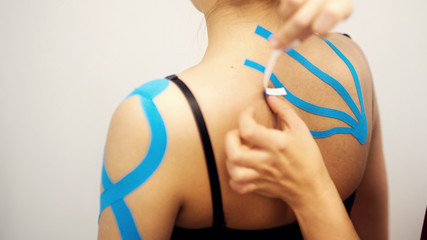 woman massage therapist applying kinesio tape to the shoulders and neck of an client in a bright...