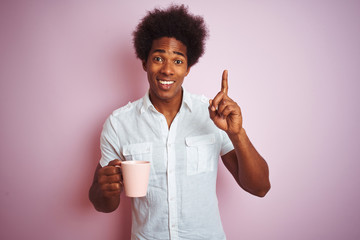 Young african american man drinking a cup of coffee standing over isolated pink background surprised with an idea or question pointing finger with happy face, number one