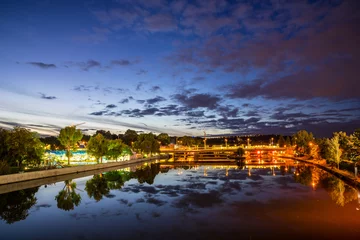 Deutschland, malerischer Blick über den glasigen Neckar, der Straßenbahn und Zug widerspiegelt, die nachts in schöner Atmosphäre am Schwimmbad von Stuttgart Bad Canstatt vorbeifahren © Simon Dux Media