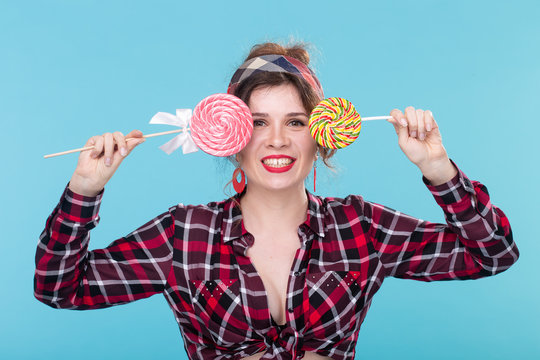 Pretty smiling young woman in a plaid shirt closes her eyes with big colorful lollipops and posing against a blue background. Concept of fun and desserts.