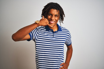 Fototapeta na wymiar Afro man with dreadlocks wearing striped blue polo standing over isolated white background smiling doing phone gesture with hand and fingers like talking on the telephone. Communicating concepts.