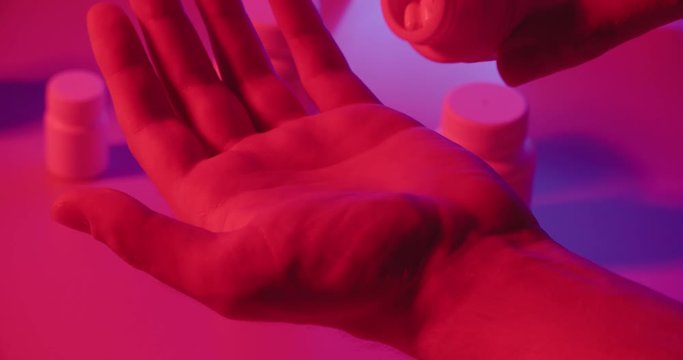Man taking pills out of can in neon light, representing modern drug and medicine addiction - Dystopia concept close up 4k footage