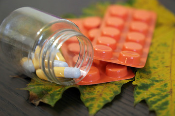 Pills on yellow maple leaf and dark wooden table, bottle of capsules and blister pack of tablets. Concept of pharmacy, antidepressants, antibiotics, vitamins for immunity in autumn cold season