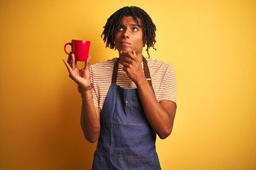Afro barista man with dreadlocks drinking cup of coffee over isolated yellow background serious face thinking about question, very confused idea