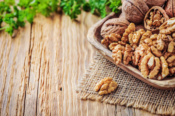 Whole walnuts in wooden bowl. Walnuts concept with green leaves on jute fabric.